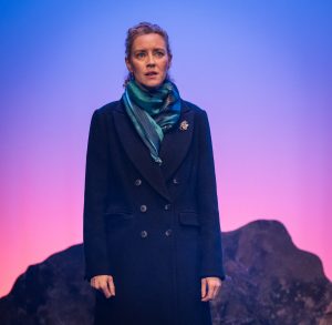 Woman Number 2 stands alone on the hillside, the colours in the background of blues, pinks and purples signifying that the sun has not long set. She is wrapped in a scarf and a heavy coat to keep out the chill of the cold Scottish evening.