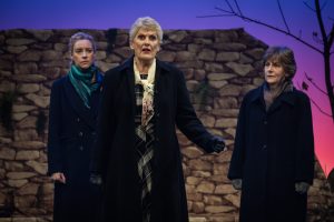 Woman Number 2 and Woman Number 1 look on from the background as Madeline continues to talk about finding her son somewhere in the hills. They know after seven years that this isn't likely - but all they can do is offer support.