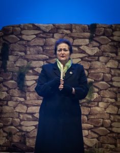 Olive played by Paola De Rosa looks off into the audience, lost in her thoughts, lit candle in hand as the candlelight vigil is held in the hills around Lockerbie.
