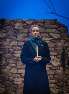 Woman Number 2 played by Frances Rowan looks off into the audience, lost in her thoughts, lit candle in hand as the candlelight vigil is held in the hills around Lockerbie.